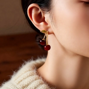 Close-up of elegant dark red cherry pendant earrings worn by a model in soft lighting
