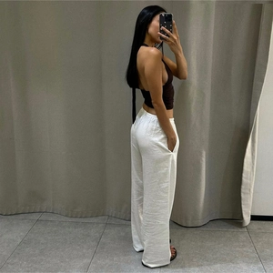 Side view of black halter backless top paired with loose white casual trousers on a model