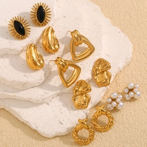 Collection of gold earrings featuring black stones, pearls, and twisted metal on stone