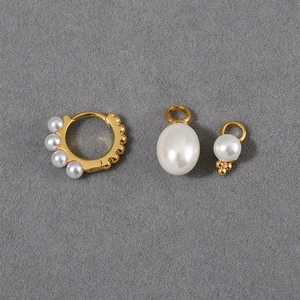 Detailed view of gold pearl hoop earrings with detachable charms on a grey background