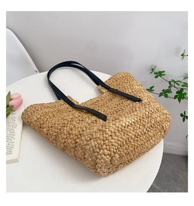 Détail du tissage de paille fait main et des bandoulières en cuir noir sur le sac