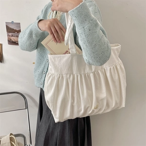 Detail of white pleated canvas tote bag showing textured cotton fabric and side logo