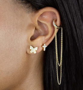 Macro shot of silver cross earrings and gold butterfly stud set with tassel chain on ear