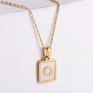 Macro detail of 18k gold plated square pendant with white shell inlay and letter O