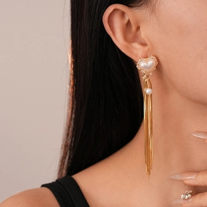 Detail of heart-shaped pearl tassel earrings with gold-plated chains worn by a model