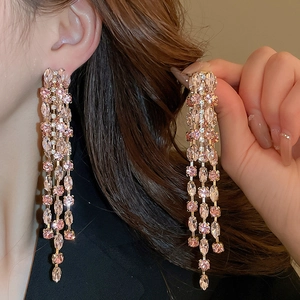 Detail of luxury long tassel earrings with pink crystals and shimmering gold finish