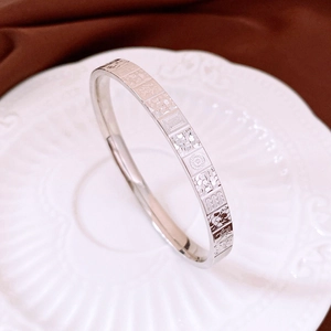Macro shot of silver metal bangle with engraved patterns on white embossed porcelain
