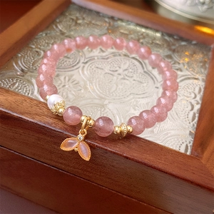 Detail of pink strawberry quartz bracelet with a pearl and golden fishtail charm on wood