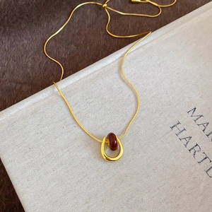 Detail of gold U-shaped pendant with deep red bead on a fine snake chain necklace
