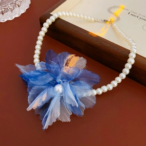 Close-up of a blue gradient fabric flower and pearl pendant on a delicate gold necklace