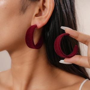 Close-up of red velvet C-shaped earrings worn and held by a model in a minimal studio