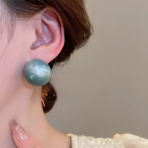 Close-up of a model wearing teal blue candy-colored round stud earrings with glossy finish