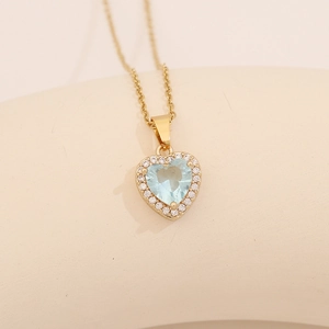 Macro shot of gold heart necklace with a light blue gemstone and zircon detailing