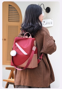 Deep red waterproof nylon backpack with plush charm worn by a model in street setting