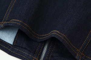 Détail d'une veste en jean indigo montrant les coutures jaunes et la fermeture éclair en métal