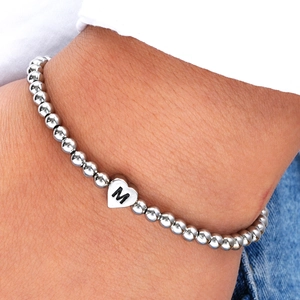 Close-up of a silver beaded heart bracelet with an engraved M initial on a model wrist