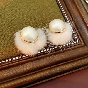 Close-up of vintage earrings featuring faux pearls, golden trim, and soft fur balls