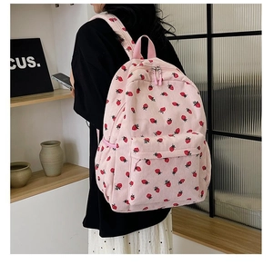 Detailed view of pink corduroy backpack with cute strawberry embroidery worn on person