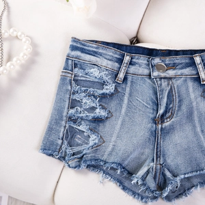 Dettaglio di pantaloncini di denim blu con strappi, orlo a frange e collana di perle