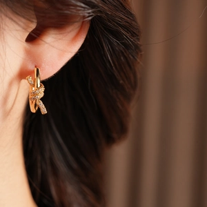 Detail of 18k gold plated knotted hoop earrings featuring sparkling zircon inlay on the earlobe