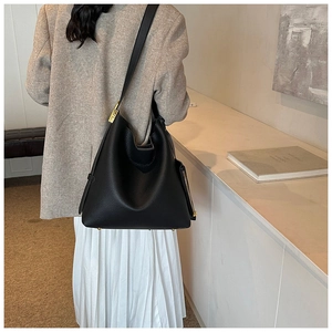 Detail of black pebbled leather tote bag with gold hardware worn by model in minimalist room