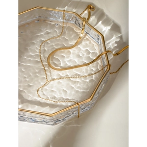 Detail of layered 18k gold stainless steel snake chain and link necklace on glass tray