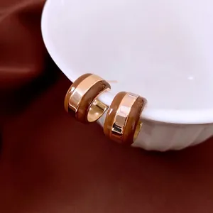 Elegant C-shaped striped gold plated earrings with brown enamel on a porcelain bowl