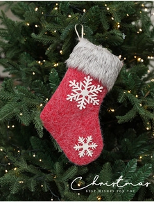 Close-up of a red felt Christmas stocking with snowflake decor on a lit Xmas tree