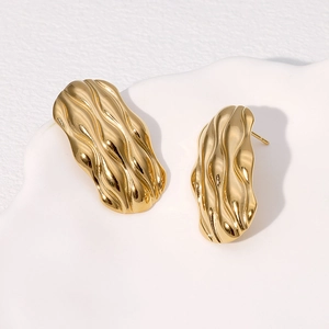 Minimalist gold wavy textured stainless steel stud earrings on a white artistic tray