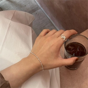 Detail of minimalist 925 sterling silver bow ring and bead bracelet on model's hand