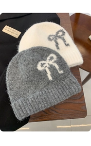 Detail of soft knit beanies in grey and beige with contrast bow patterns and plush texture