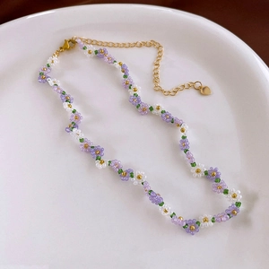 Macro detail of handmade beaded flower necklace with purple daisy patterns and gold clasp