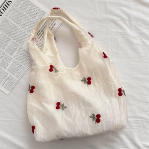 Detail shot of delicate cherry embroidery on a white mesh tote bag with a soft aesthetic