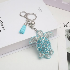 Blue rhinestone sea turtle keychain with leather shell and tassel on a white book