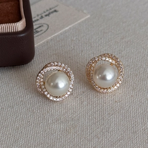 Detailed view of pearl stud earrings with sparkling cubic zirconia on beige fabric