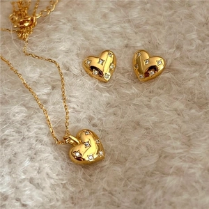 Detail of gold heart necklace and earrings set with white zircon on plush background