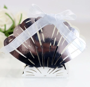 Macro detail of glossy silver shell-shaped wedding favor box with a white silk ribbon bow