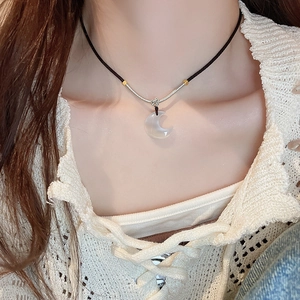 Close-up of white crescent moon pendant on black cord worn on a model's neck