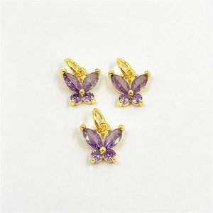 Détail de trois pendentifs papillon en laiton doré ornés de zircons violets brillants