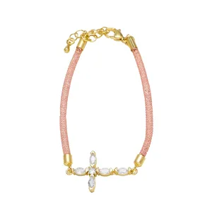 Detalle de pulsera de cruz dorada con circonitas marquise y correa de malla trenzada rosa