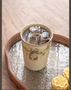 Macro detail of Ru kiln ceramic cat mug with ice cubes and flowers on wooden tray