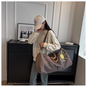 On-model shot of a large brown canvas travel bag with playful hand-drawn graffiti patterns