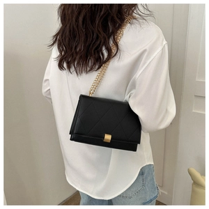 Quilted black shoulder bag with gold chain strap worn by a model in casual outfit