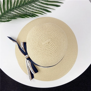 Détail du tressage fin en paille et du ruban bleu marine avec nœud sur le chapeau d'été