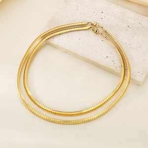 Close-up of 18K gold plated flat snake chain necklaces on a textured stone display