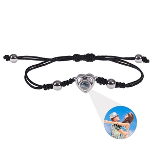 Detail of black braided bracelet featuring a silver heart charm with photo projection lens