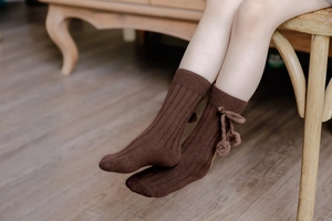 Detail of coffee brown ribbed knee-high baby socks with decorative pom-pom tassels