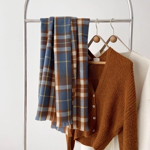 Close-up of thick plaid scarf texture with a brown knit cardigan on a wooden hanger