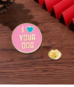 Close-up of pink and gold enamel brooch with I Heart Your Dog text on wood background