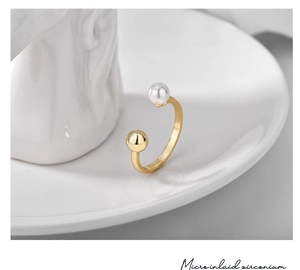 Detailed view of gold open ring with shell pearl and micro-inlaid zircon on white ceramic tray